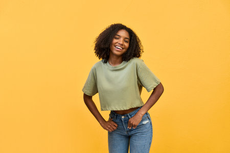 Young happy African American gen z teen girl standing at yellow wall. Portrait.の写真素材