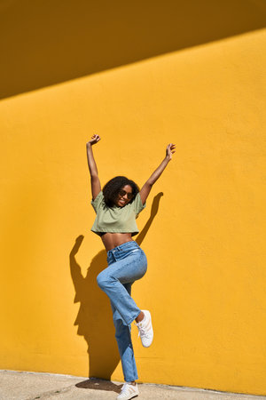 Happy young African American woman winner jumping standing at yellow wall.の写真素材