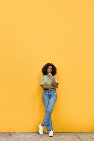 Young happy African American gen z teen girl standing at yellow wall. Full body.の写真素材