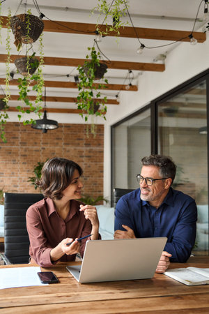 Two happy business team people using laptop working together at office meeting.