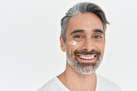 Happy middle aged man applying facial cream isolated on white studio background.の写真素材