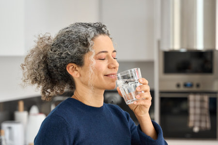Healthy happy woman of middle age holding glass drinking water at home.