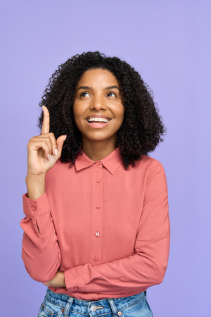 Happy young African woman pointing finger up isolated on purple background.
