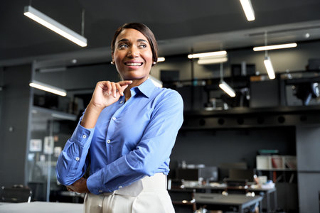 Young confident African American business woman standing in office looking away.