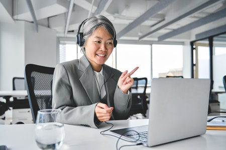Happy older Asian business woman having virtual meeting working using laptop.の写真素材