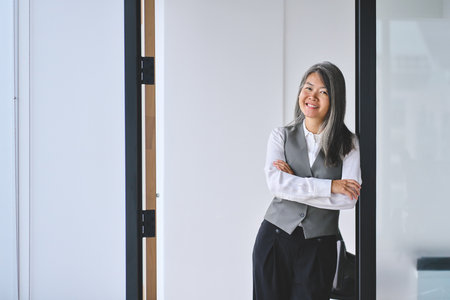 Middle aged Asian business woman standing in office arms crossed. Portrait.の写真素材