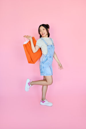 Happy young Asian woman looking inside shopping bag isolated on pink.の写真素材