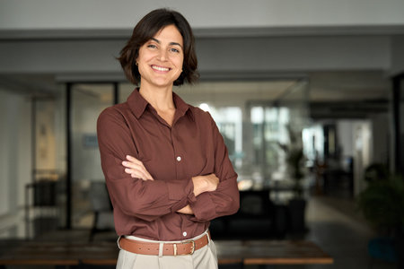 Happy young business woman standing in office arms crossed looking at camera.の写真素材