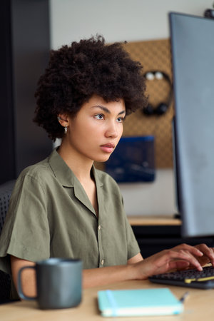 Young African woman student using pc computer sitting at desk. Vertical.