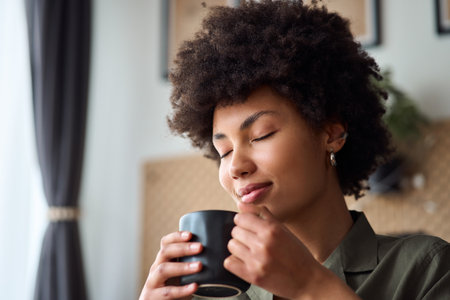 Young happy African American woman holding cup drinking coffee relaxing at home.の写真素材