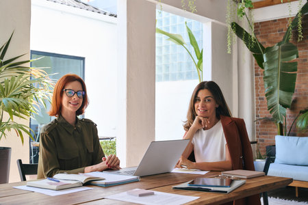 Portrait of two happy business women sitting at work desk with laptop.の写真素材