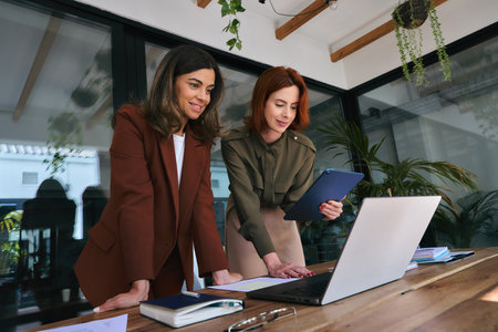 Two happy business women of young and middle age working on laptop in office.の写真素材