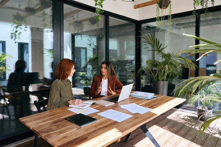 Two busy business women young and middle aged talking working in green office.の写真素材