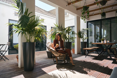 Happy mature business woman using phone sitting in chair in sunny green office.の写真素材