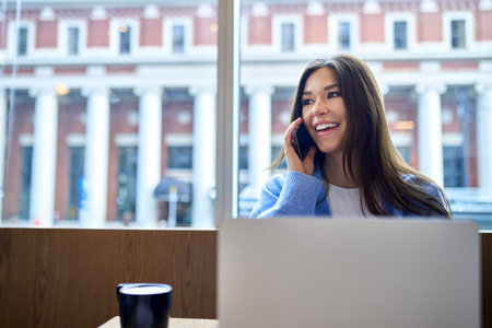 Young happy business woman or student using laptop talking on the phone.