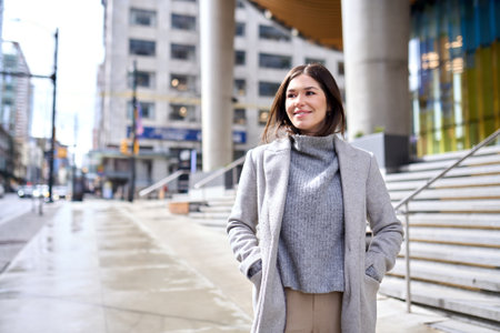 Young happy woman wearing coat walking on city street on sunny day.