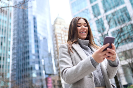 Young happy woman using mobile phone standing on city street.の写真素材
