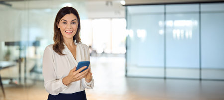 Mid aged happy professional business woman using phone at office, portrait.の写真素材