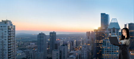 Young Asian business woman holding laptop standing at night office window.の写真素材