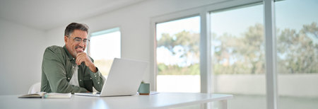 Happy older mature man using laptop computer at home table.