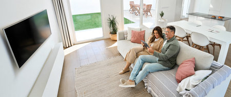 Happy mature old couple hugging sitting on sofa at home using digital tablet.