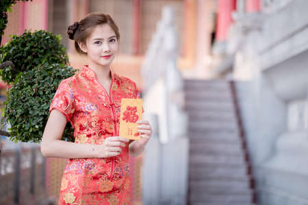 Asian woman in chinese dress holding couplet 'Happy
' (Chinese word) with chinese temple background.の写真素材