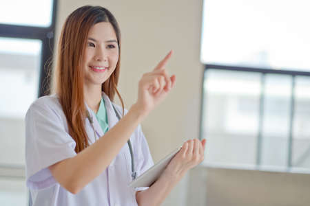 Happy smiling young beautiful female doctor showing blank area for sign or copyspaceの写真素材