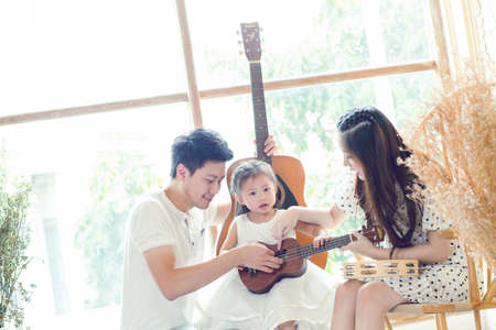 Father, mother daughter playing music at home with guitarの写真素材