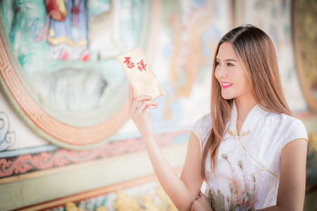 Asian woman in chinese dress holding couplet 'Happy' (Chinese word) with chinese temple background.の写真素材