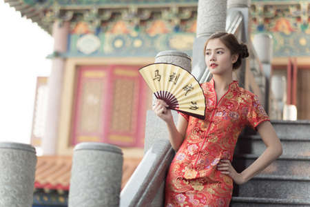Asian woman in chinese dress holding couplet 'success' (Chinese word) with chinese temple background.の写真素材