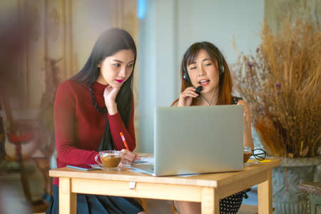 Asian young business woman use laptop sitting at wooden table of modern coffee shopの写真素材
