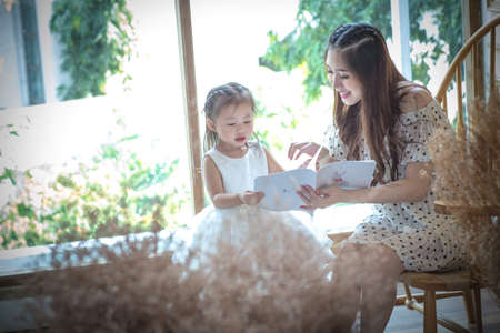 family, children, education, school and happy people concept - happy mother and daughter reading...