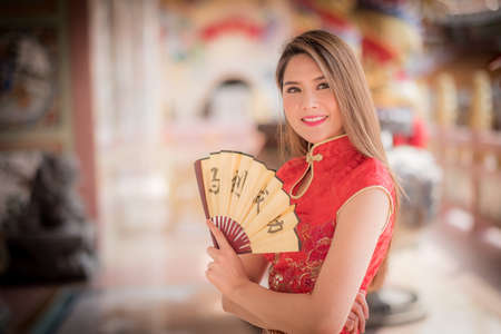 Asian woman in chinese dress holding couplet 'success' (Chinese word) with chinese temple background.の写真素材