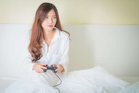 Portrait of a cute girl playing video games while she is lying on her bed,Lighting with sun flareの写真素材