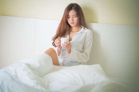 Beautiful brunette woman drinking and morning coffee in bedroom ,Lighting with sun flareの写真素材
