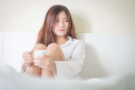 Beautiful brunette woman drinking and morning coffee in bedroom ,Lighting with sun flareの写真素材