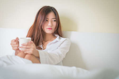 Beautiful brunette woman drinking and morning coffee in bedroom ,Lighting with sun flareの写真素材