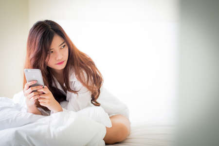 girl using a mobile phone lying on the bed at home,Lighting with sun flareの写真素材