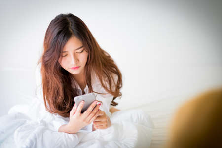 girl using a mobile phone lying on the bed at home,Lighting with sun flareの写真素材