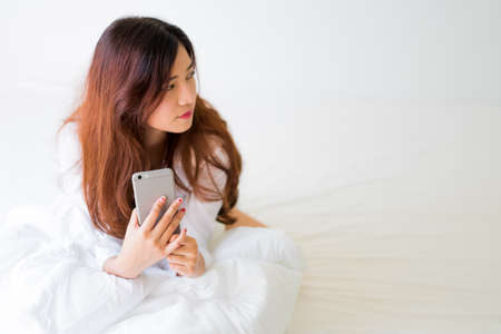 girl using a mobile phone lying on the bed at home,Lighting with sun flareの写真素材