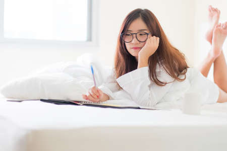 Smiling woman writing notes lying in bed ,Lighting with sun flareの写真素材