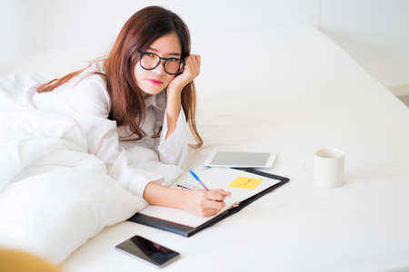 Smiling woman writing notes lying in bed ,Lighting with sun flareの写真素材