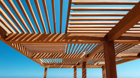 Elegant outdoor pergola made of warm-toned wooden slats, minimalist design blending with nature, sunlight streaming through beams against vivid skyの素材