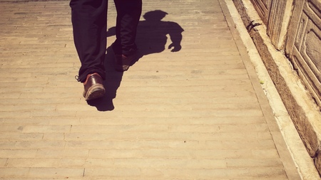 Traveling man walking on an ancient city sidewalk (in China). The image was taken from waist down with shadow of the whole body; retro style; bottom copy space for textの写真素材