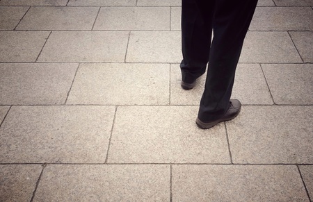 Business man standing on an city sidewalk; taken from hip down and behind; wearing black trousers and brown shoes; retro style; copy space on left.の写真素材