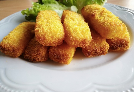 Perspective view of crisp fish fingers (or fish sticks) on a white plate; with hydroponics vegetables ( red and green lettuce oaks) on background. Bottom blurred area of plate is copy-space for add text.の写真素材