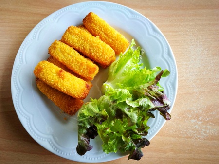 Top view of crispy fish fingers sticks and red green oak (lettuce) vegetables on a white plate (put on old wooden table); copy space on the right.の写真素材