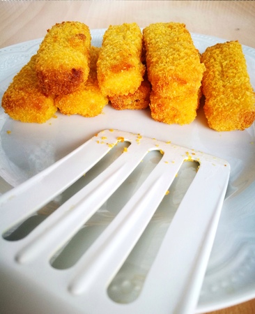 Close-up of crisp fish fingers are on a white plate and put on wooden table - Perspective view taken from handle of the food flipper. Blurred part of flipper is foreground and can be used as copy-space for add text. Concept of newly fried food.の写真素材
