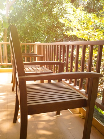 Two wooden chairs and one table on balcony in summer with natural trees background. The image was shot in side view and add light flare. Use as visual content in concept of outdoor relaxation, restful area, etc.の写真素材