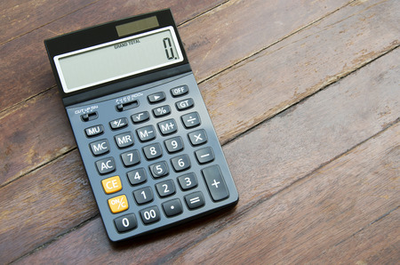 Press the button on the calculator with a wooden floor in the background.の写真素材